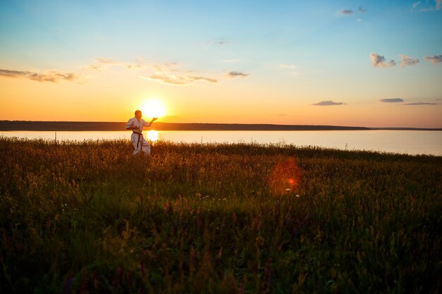 Silhouette of sportive man training karate in field at sunrise.