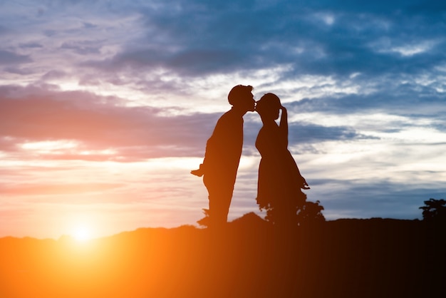 Silhouette of sweet couple kissing over sunset background.