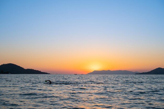 Silhouette of a swimmer exercising in the sea against the backdrop of a sunset over the bay the idea for a screensaver or advertisement for a vacation at sea