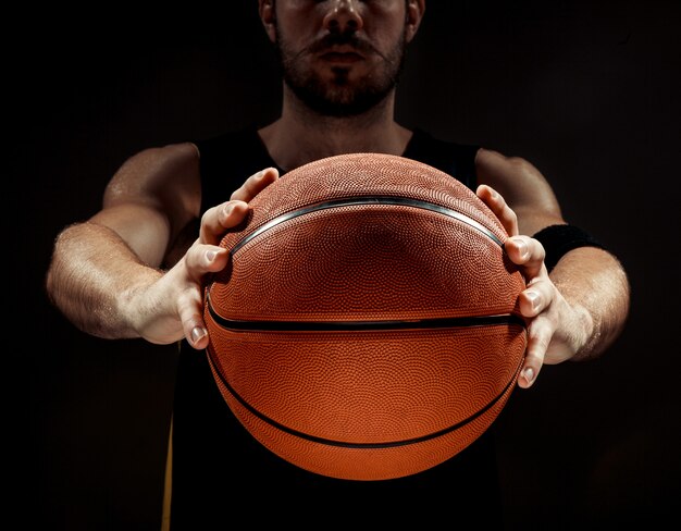 黒の背景にバスケットボールを保持しているバスケットボール選手のシルエットビュー