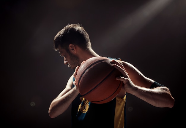 黒い空間にバスケットボールを保持しているバスケットボール選手のシルエットビュー