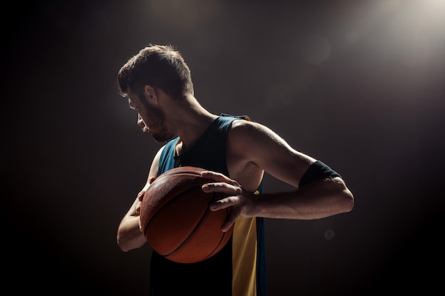 Силуэт вид баскетболиста, держащего баскетбольный мяч на черной стене