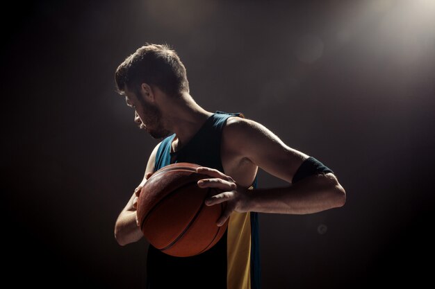 黒い壁にバスケットボールを保持しているバスケットボール選手のシルエットビュー