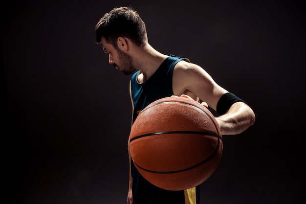 Силуэт вид баскетболиста, держащего баскетбольный мяч на черном