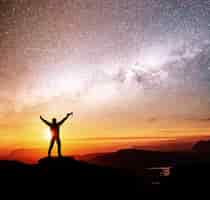 Free photo silhouette of woman is standing on top of mountain and pointing to the milky way before sunrise and enjoying with colorful night sky