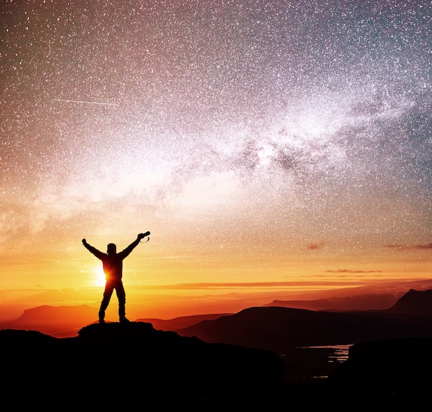 Silhouette of woman is standing on top of mountain and pointing to The milky way before sunrise and enjoying with colorful night sky