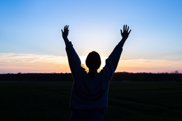 Free photo silhouette of a woman at sunset in a field against the sky rear view