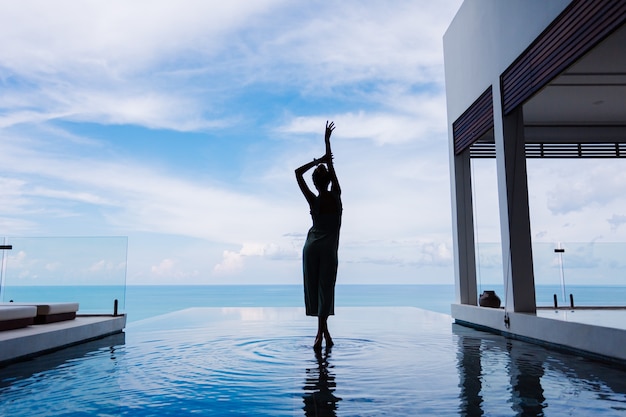 Silhouette of a woman walking on the water surface of the infinity pool of an expensive rich luxury villa on a mountain with a sea view