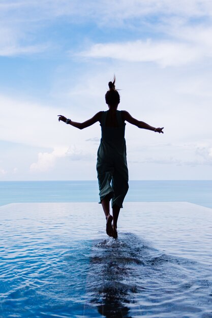 Silhouette of a woman walking on the water surface of the infinity pool of an expensive rich luxury villa on a mountain with a sea view