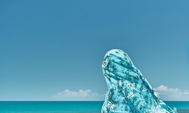 Silhouette of a woman wrapped in a scarf against a gust of wind against the background of the summer sea and blue clear sky weekend at sea cool breeze