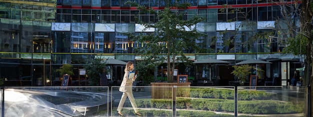 Free photo silhouette of young business woman in beige suit walking in city center posing near office buildings