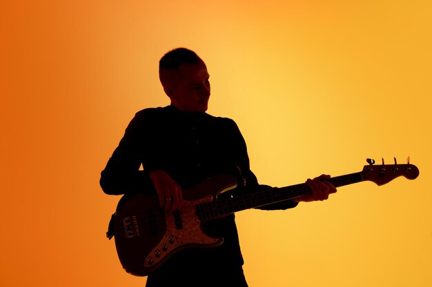 Silhouette of young caucasian male guitarist isolated on blue-pink gradient studio in neon light