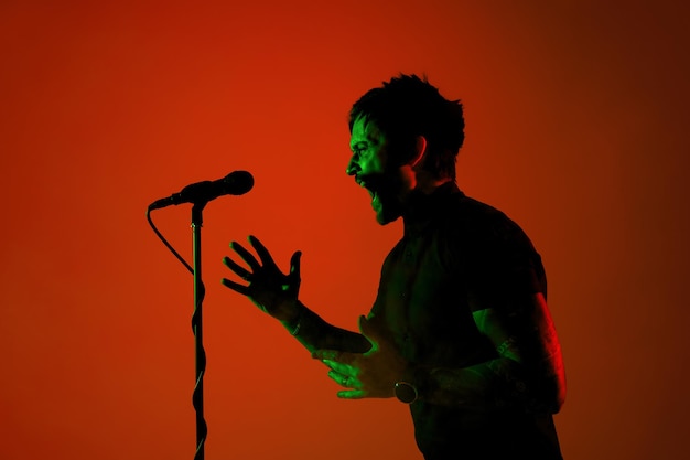 Silhouette of young caucasian male guitarist isolated on blue-pink gradient studio in neon light