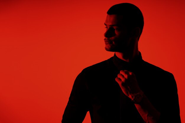Silhouette of a young confident handsome businessman wearing black shirt in red light