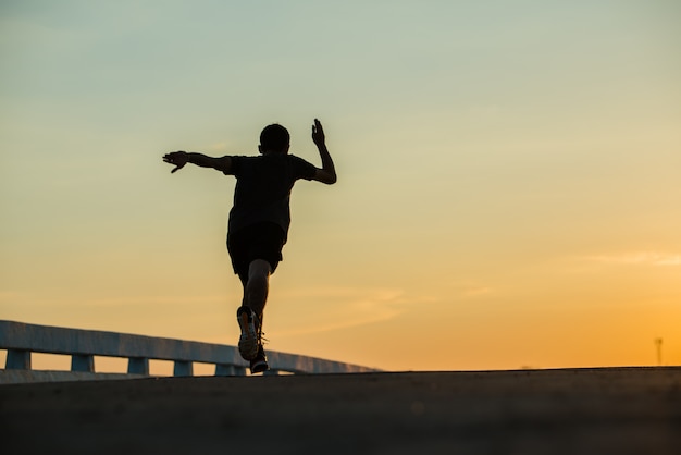 日の出を走っている若いフィットネス男のシルエット