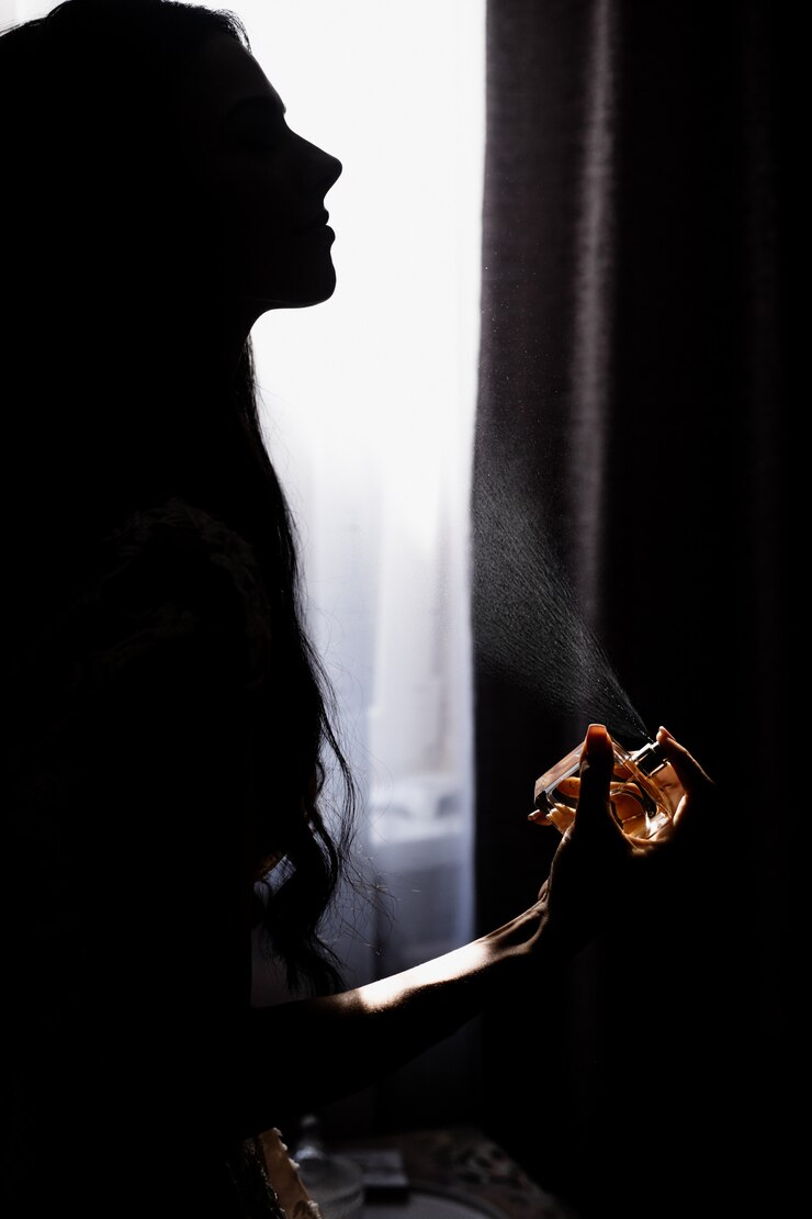 Free Photo silhouette of young girl who is perfuming in front of window in darkness