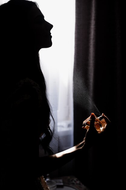 暗闇の中で窓の前で香水している若い女の子のシルエット