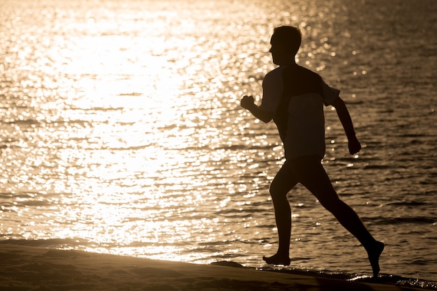 海岸でジョギングする若い男性のシルエット
