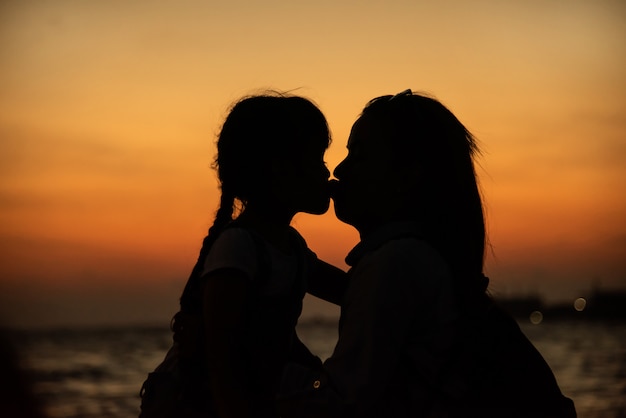Silhouette of a young mother lovingly kissing her little daughter