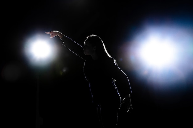 Silhouette of young woman gesturing isolated on black wall with flashlights. Copyspace.