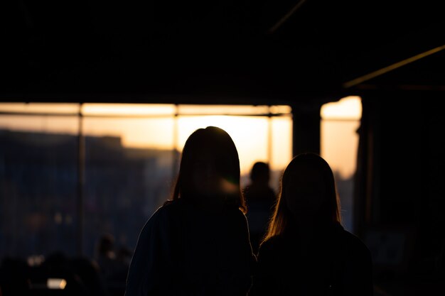 Silhouettes of girls looking out the window at the sunset, view from the back.