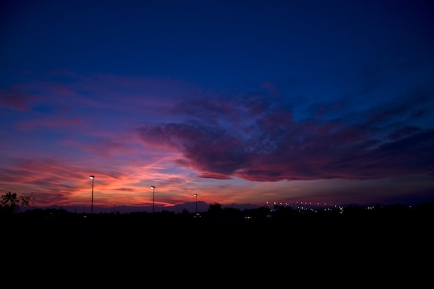 美しい夕日の曇り空の下で丘と街灯のシルエット