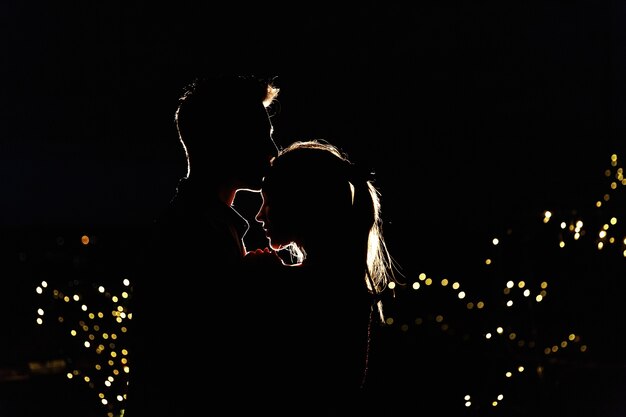 夜の屋上に立っている素敵な若いカップルのシルエット