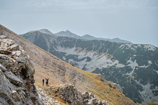 Silhouettes of man and woman against backdrop of mountains rejoice at success active recreation