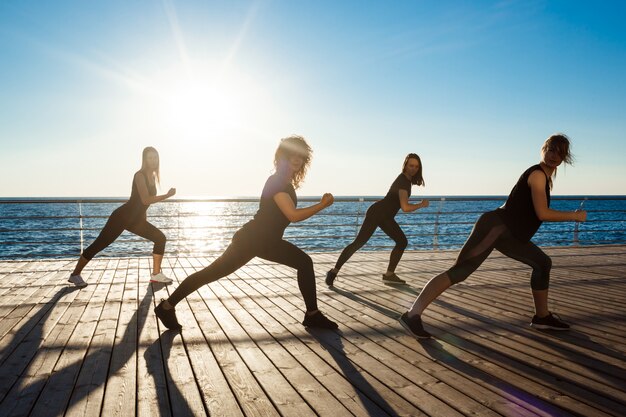 日の出の海のそばで踊る陽気な女性のシルエット