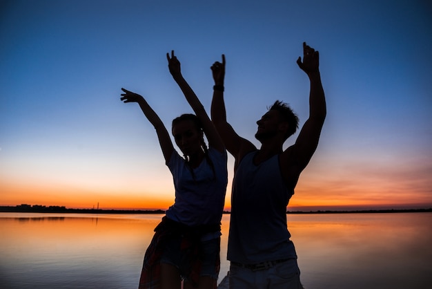 Free photo silhouettes of young beautiful couple resting rejoicing at sunrise near lake