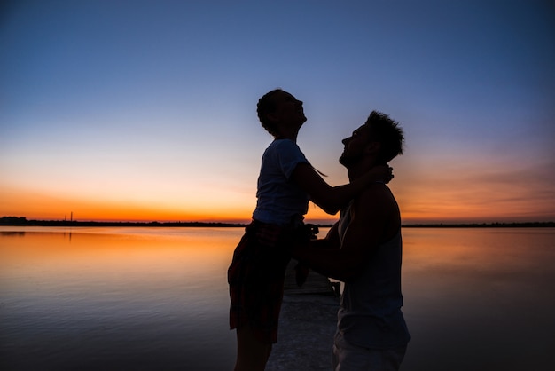 Silhouettes of young beautiful couple resting rejoicing at sunrise near lake