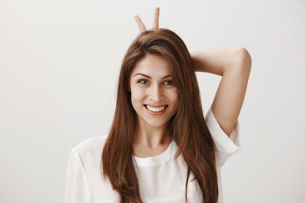 Silly adorable girl showing bunny gesture and smiling happy