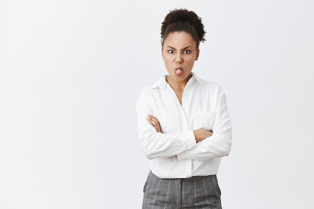 Silly and childish cute african-american female in white shirt showing tongue, looking offended