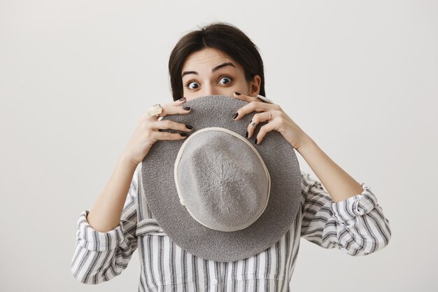 silly cute brunette female hiding face behind hat and peeking
