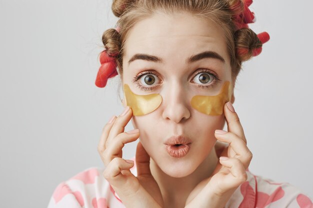 Silly cute girl in hair curlers and nightwear apply eye patches