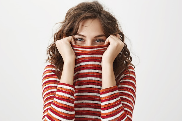 Foto gratuita ragazza carina sciocca che si nasconde all'interno del maglione, sorridente con gli occhi