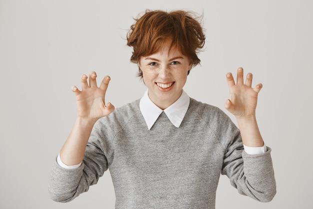 Silly and funny redhead girl with short haircut posing against the white wall