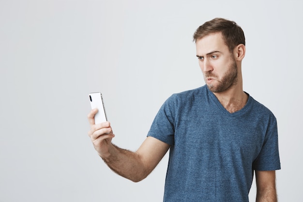 Silly handsome guy taking selfie on smartphone, pouting