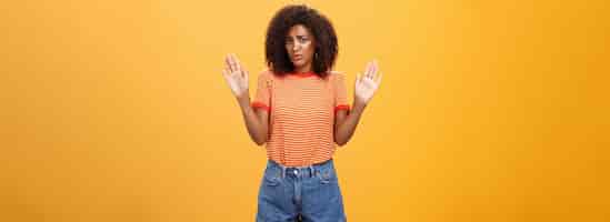 Free photo silly insecure and sad darkskinned female model in trendy striped tshirt and shorts raising arms in