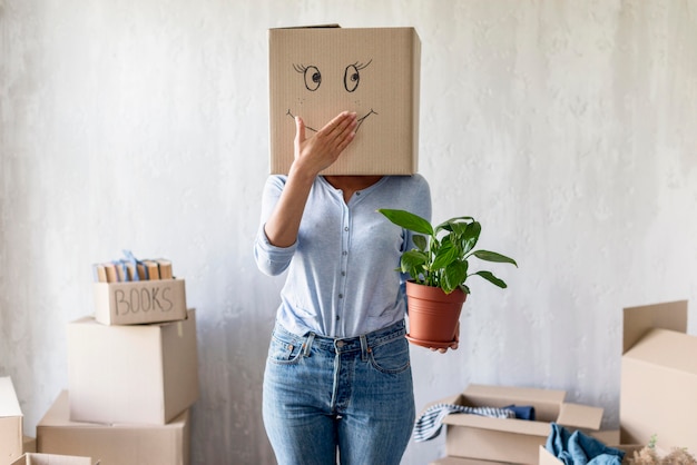 愚かな女性がボックスを頭の上でポーズし、移動する荷造りしながら手に植物