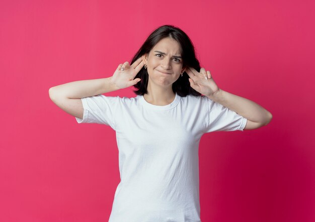 Silly young pretty caucasian girl making monkey ears isolated on crimson background