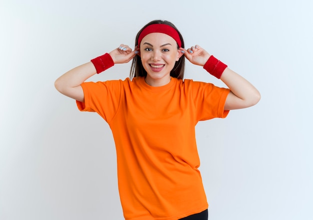 Foto gratuita sciocca giovane donna sportiva indossando la fascia e braccialetti sorridenti che fanno grandi orecchie isolate