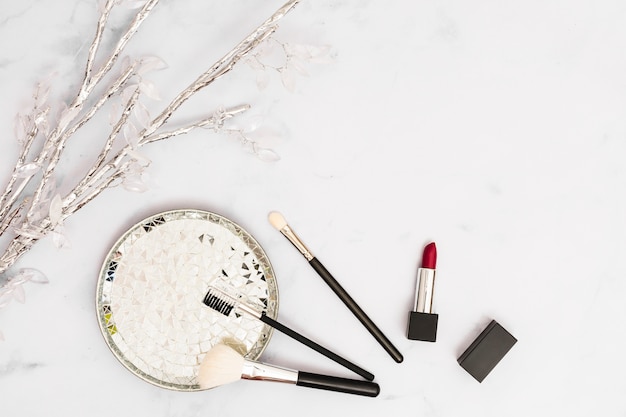 Silver and crystal branch with plate; makeup brushes and lipstick on white background