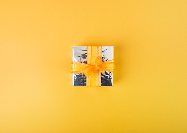 Free photo silver gift box decorated with ribbon on yellow background