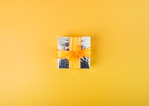 Silver gift box decorated with ribbon on yellow background