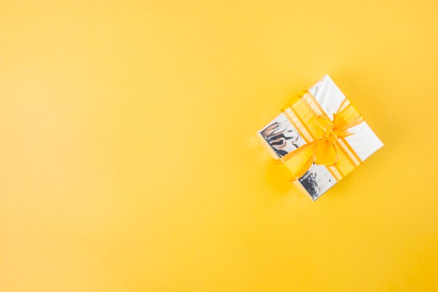 Silver gift box decorated with yellow ribbon over the yellow background