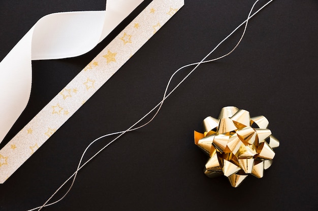 Free photo silver string; white and star shape ribbon and golden bow on black background