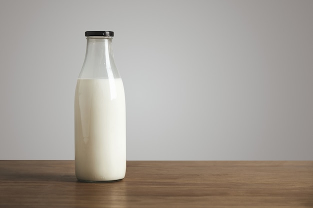 Simple vintage bottle filled with fresh milk on thick wooden table. Closed with black cap. Cafe shop