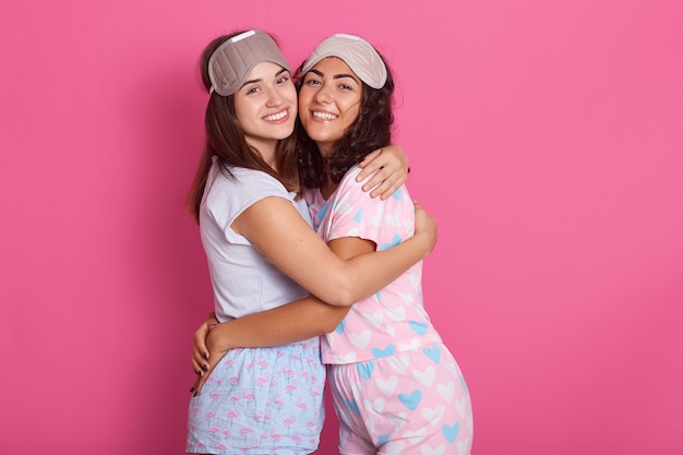 sincere beautiful friends posing isolated over pink, hugging each other, smiling