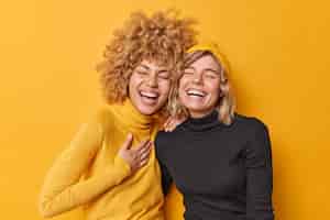 Free photo sincere human emotions concept positive overjoyed young women have fun laugh gladfully smile toothily cannot stop laughing stand closely to each other dressed casually isolated over yellow wall
